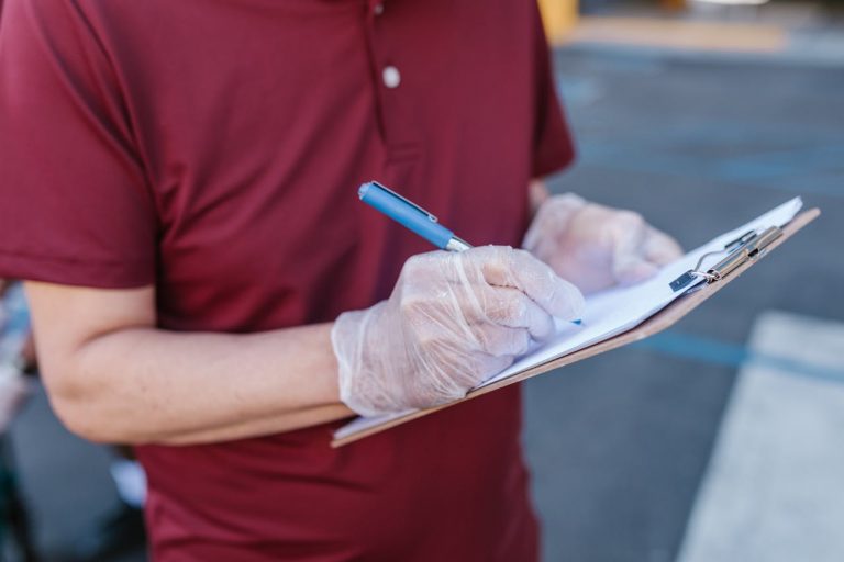 Person hält Klemmbrett und schreibt mit Stift auf Papier